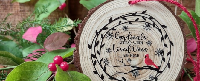 A wood-slice, rustic ornament with a vine, snowflakes, a cardinal, and the phrase "cardinals appear when loved ones are near."